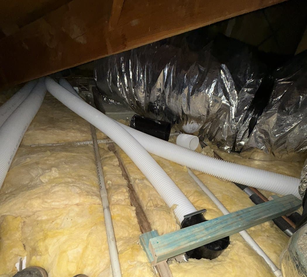 Flexible ComfoTube ducting and insulated rigid ducting routed through an existing roof cavity during an MVHR retrofit, photographed before R5 insulation batts were laid back over the run